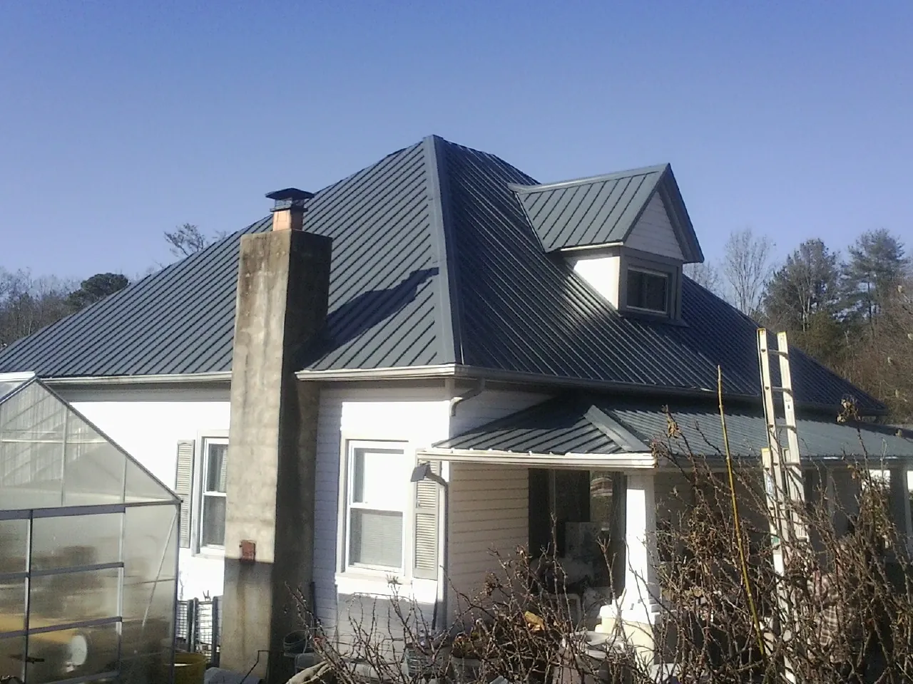 Dark blue standing seam metal roof on a white farmhouse with dormer — Slate & Tile Roof Repair by Roofing Brothers in Cortez