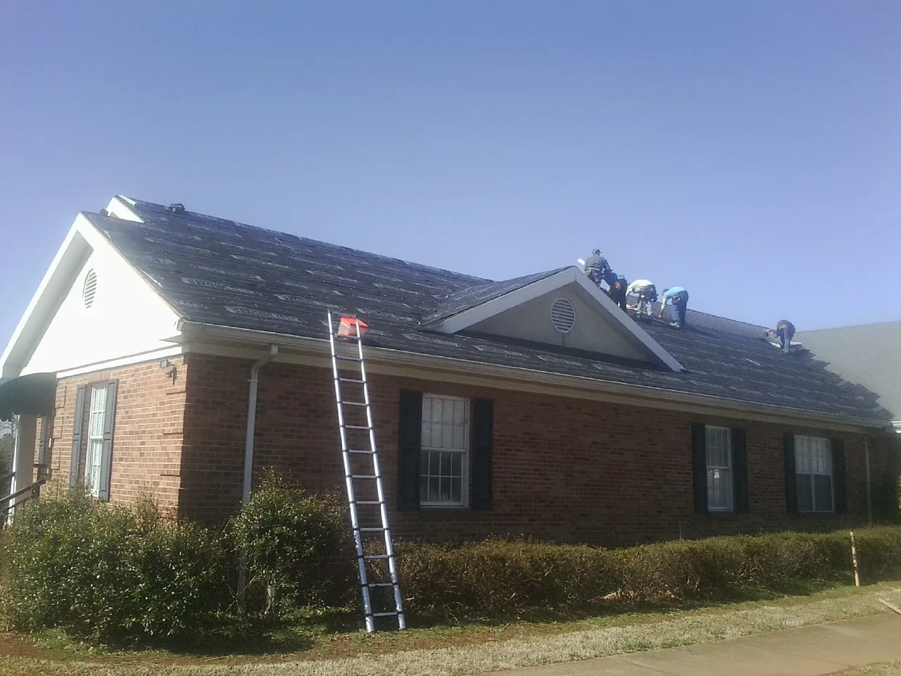 Crew tearing shingles off a brick ranch roof with a ladder set — Metal Roof Repair work by our crew in Cortez