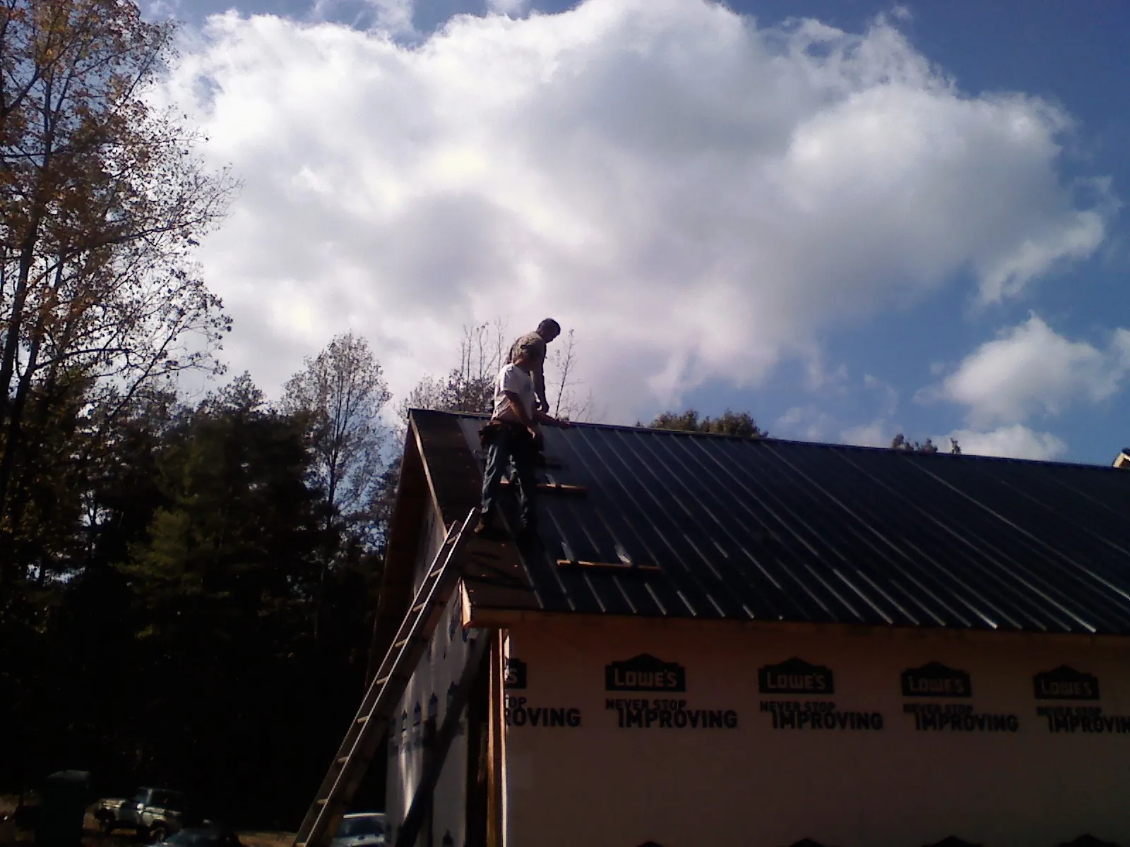 Roofer fastening dark metal panels high against a cloudy sky, from a Roof Inspection job in Cortez