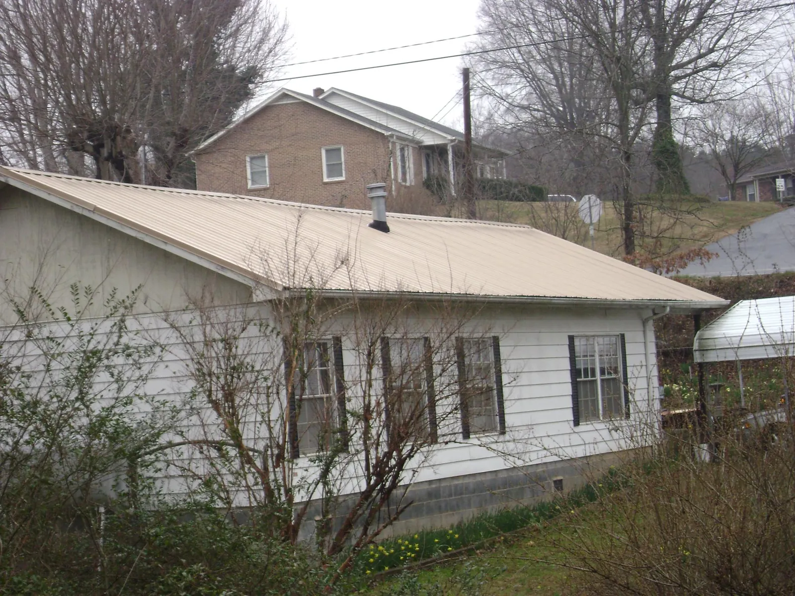 Tan metal roof on a white sided house set into a hillside — Commercial Roofing by Roofing Brothers in Cortez